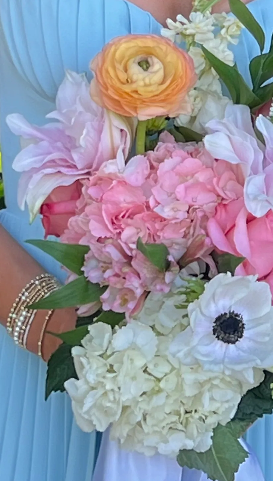 Bouquet of pink hydrangea, white anemones, orange ranunculus and a calla lily against a pale blue gown